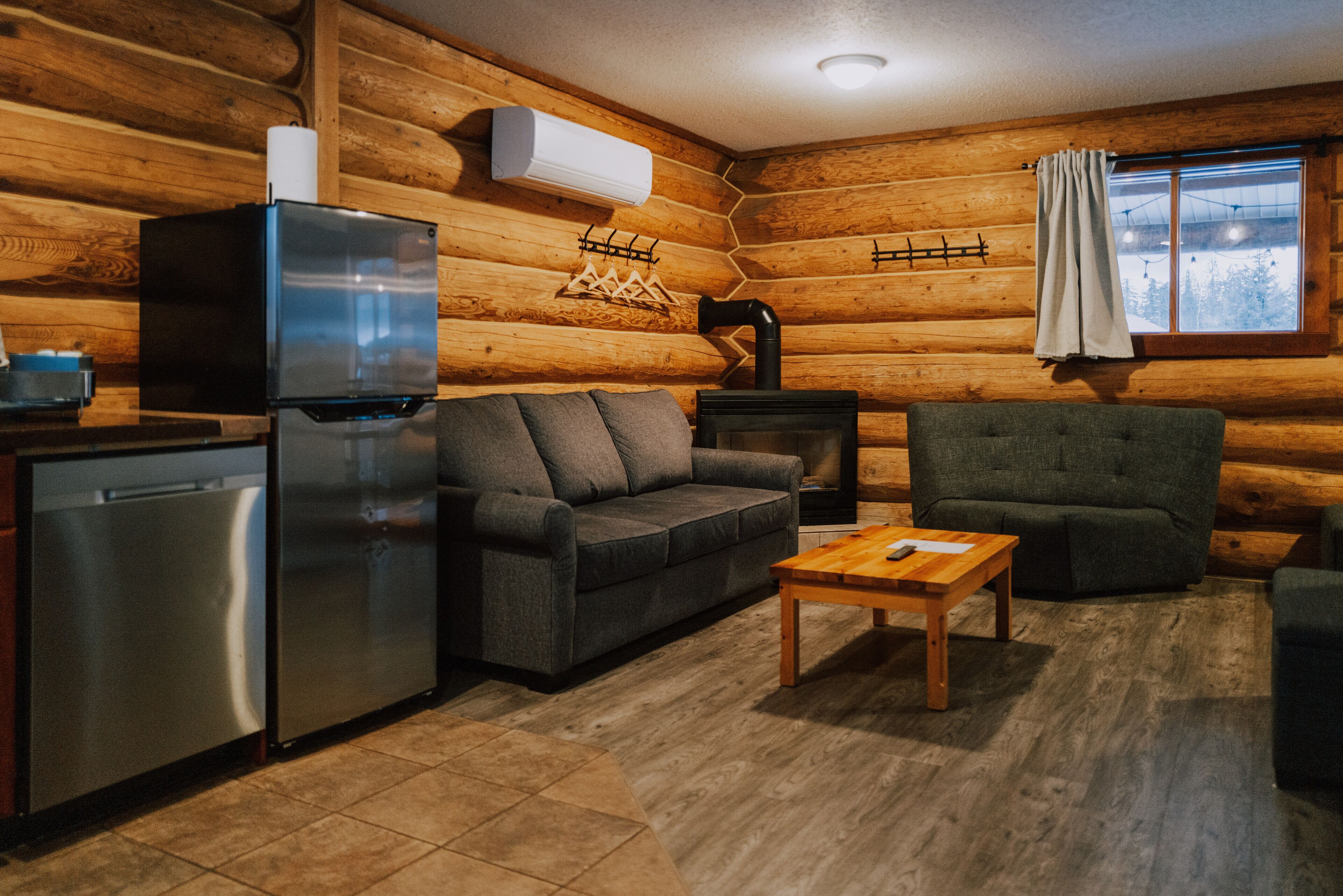 L’intérieur d’une cabane en rondins, avec un canapé, un fauteuil, une table basse en bois et un poêle à bois encastré.