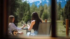 Dos personas sentadas a una mesa con un perro, con vistas a un paisaje montañoso.