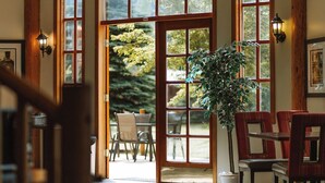 Una habitación con ventanas amplias, paredes de madera, una zona de comedor con sillas y una planta en maceta.