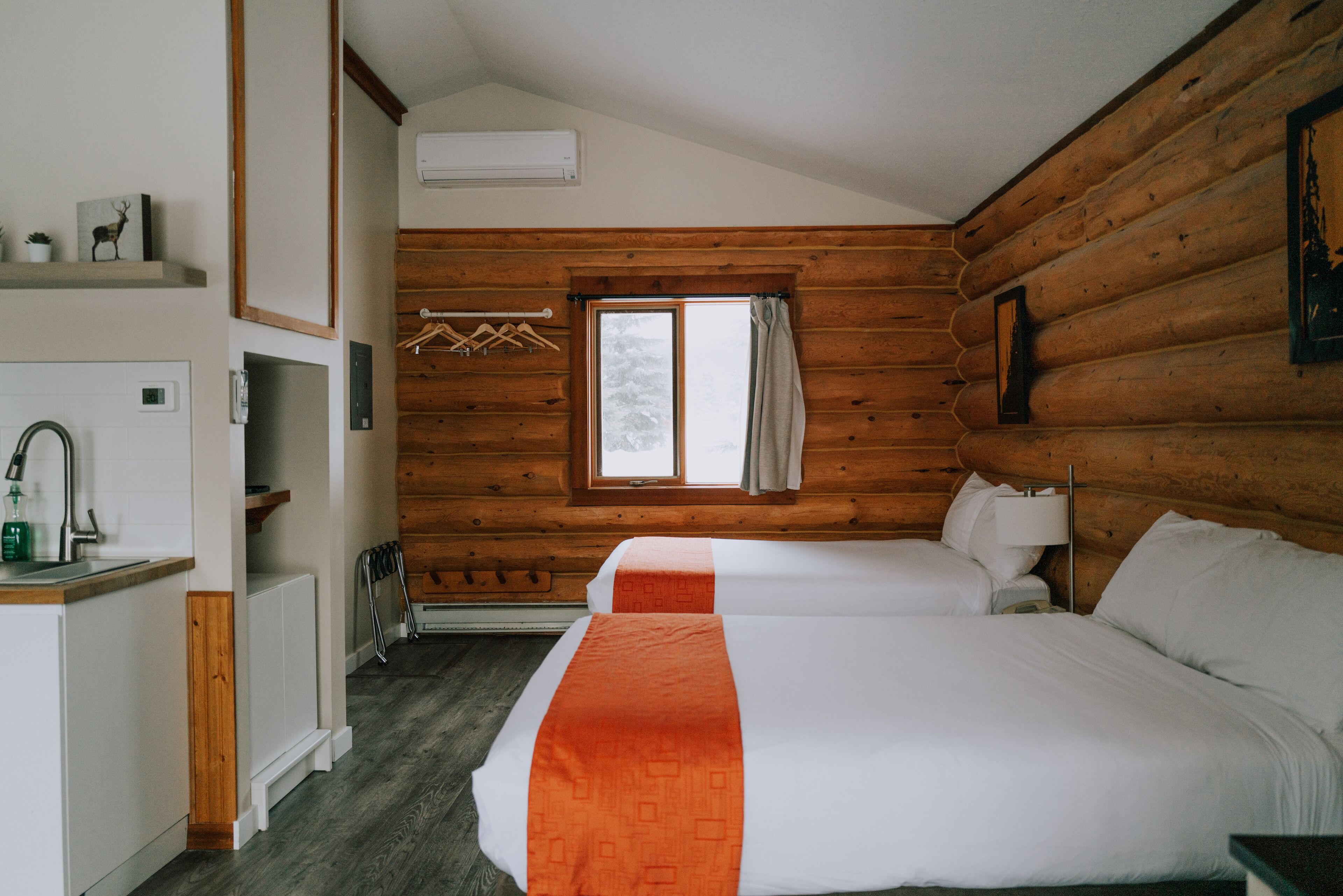 A log cabin-style room with two beds, a small kitchenette, and a window with a view of the outdoors.