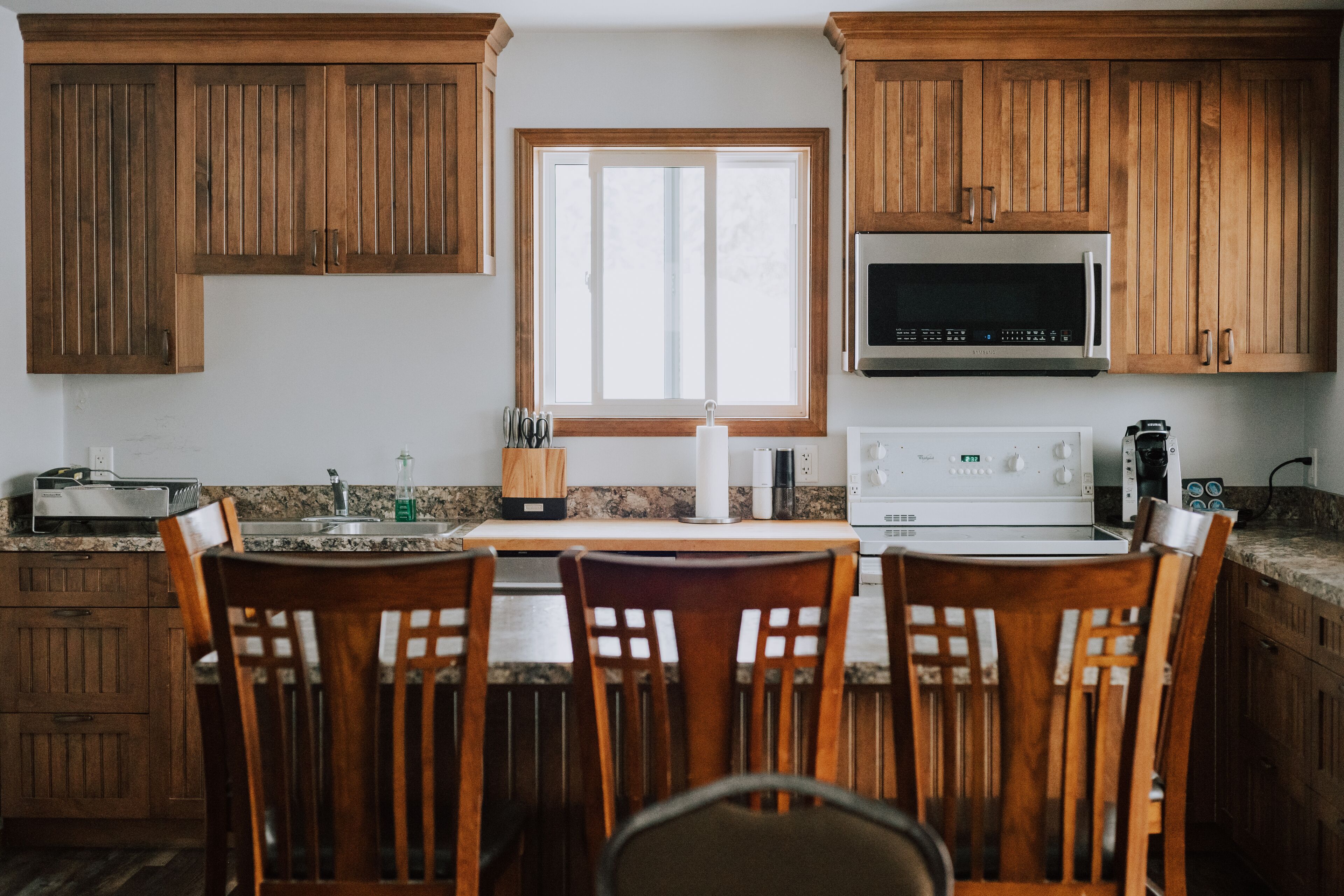 A kitchen with wooden cabinets, a window, a microwave, a toaster, and a sink.