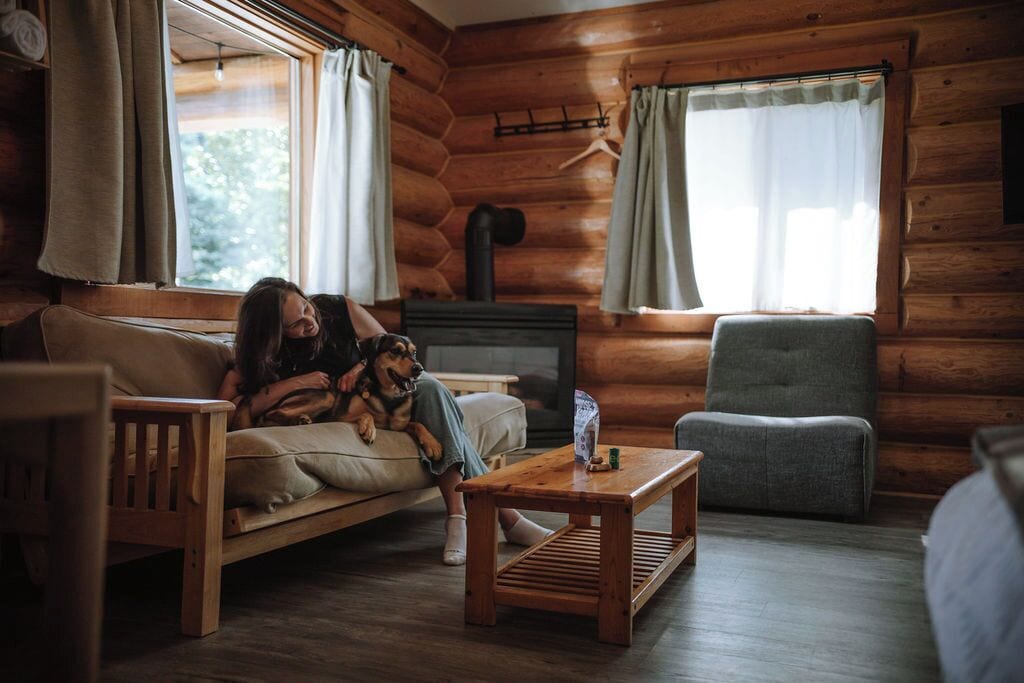 A log cabin interior with a sofa, a wooden coffee table, a television, and a chair.