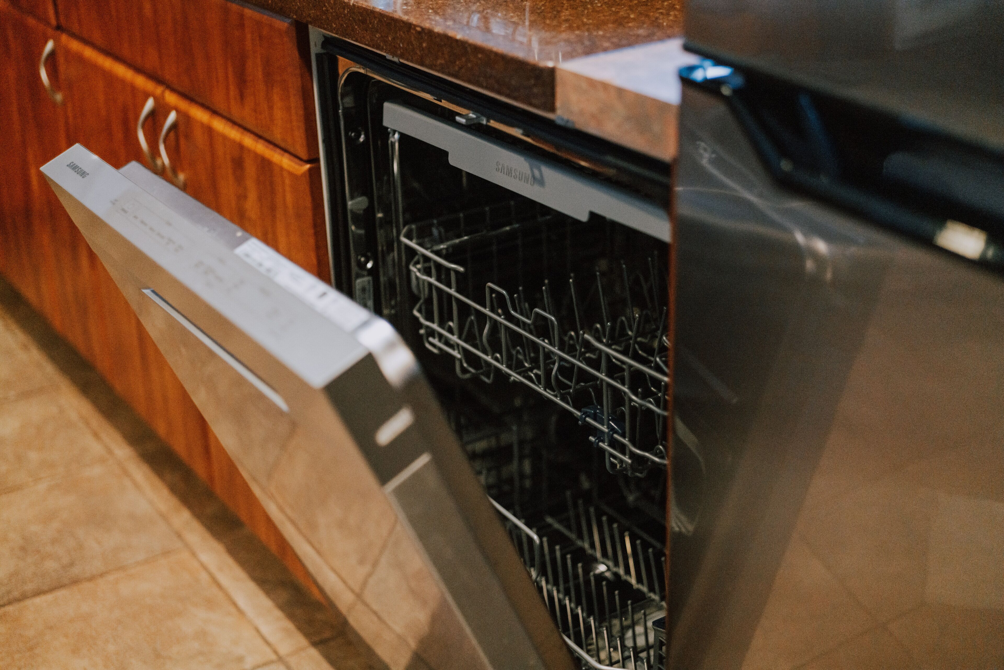 A stainless steel dishwasher in a kitchen with wooden cabinets and a granite countertop.