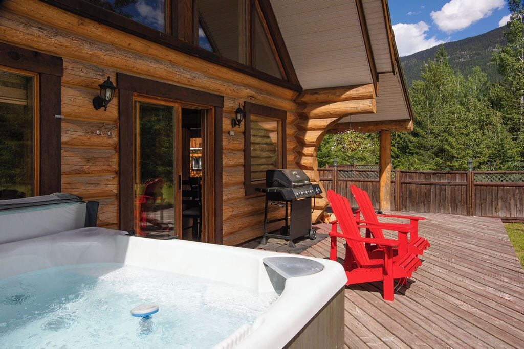 A wooden cabin with a hot tub, outdoor seating, and a grill.