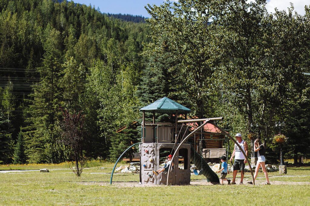 A playground with climbing structures and a small shelter, surrounded by trees and a hilly landscape.