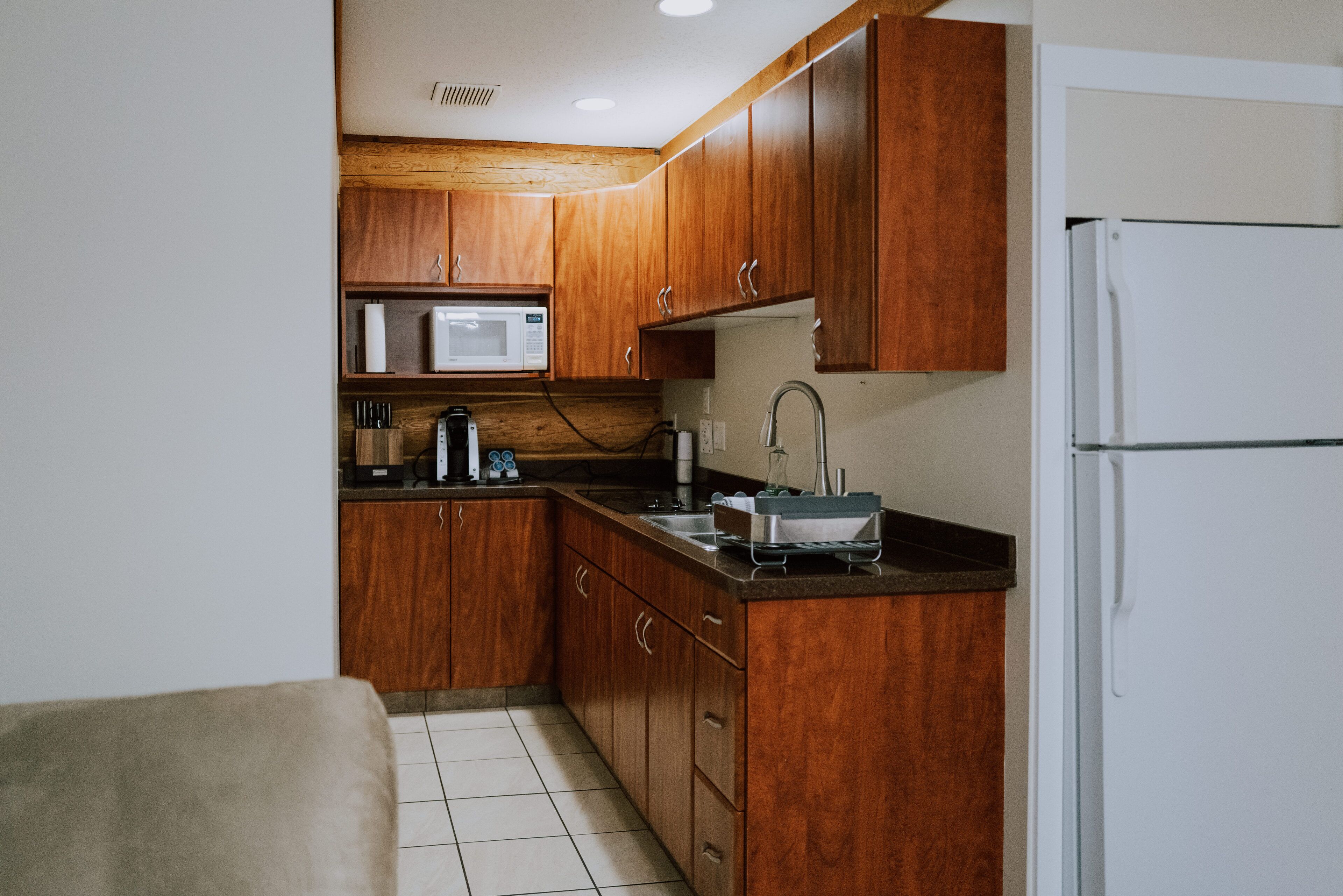 A compact kitchen with wooden cabinets, a microwave, a sink, and a refrigerator.