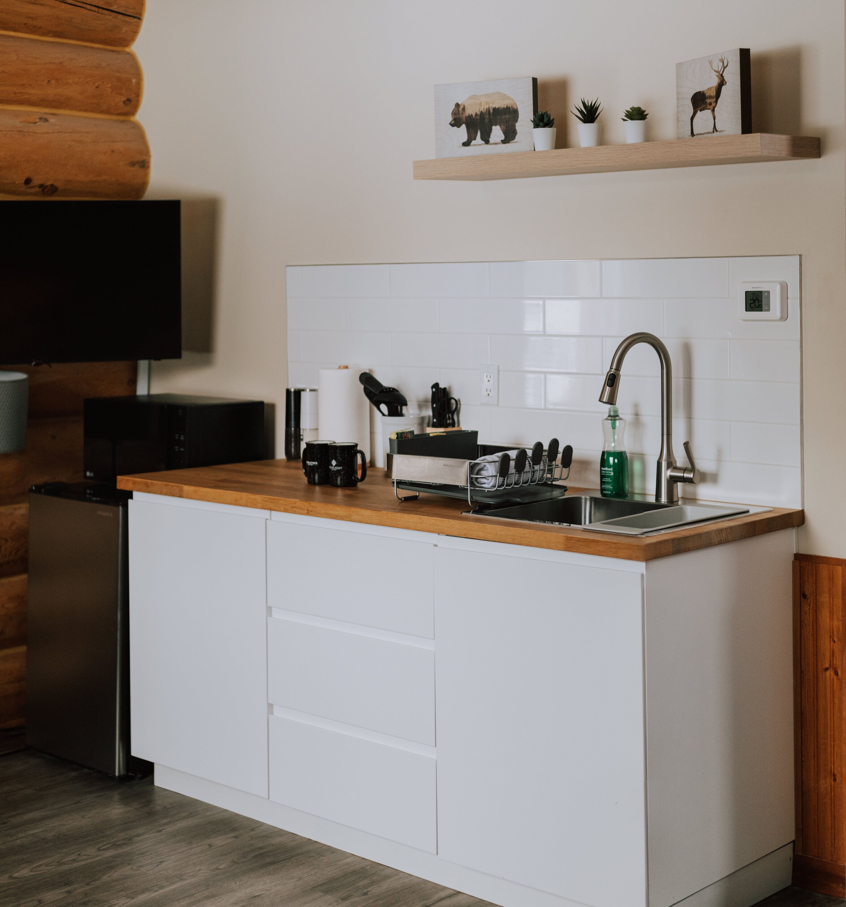 A compact kitchen with a wooden countertop, white cabinets, a built-in sink, and a mounted television.