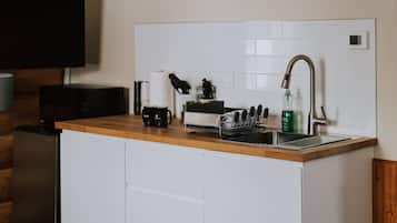 A compact kitchen with a wooden countertop, white cabinets, a built-in sink, and a mounted television.