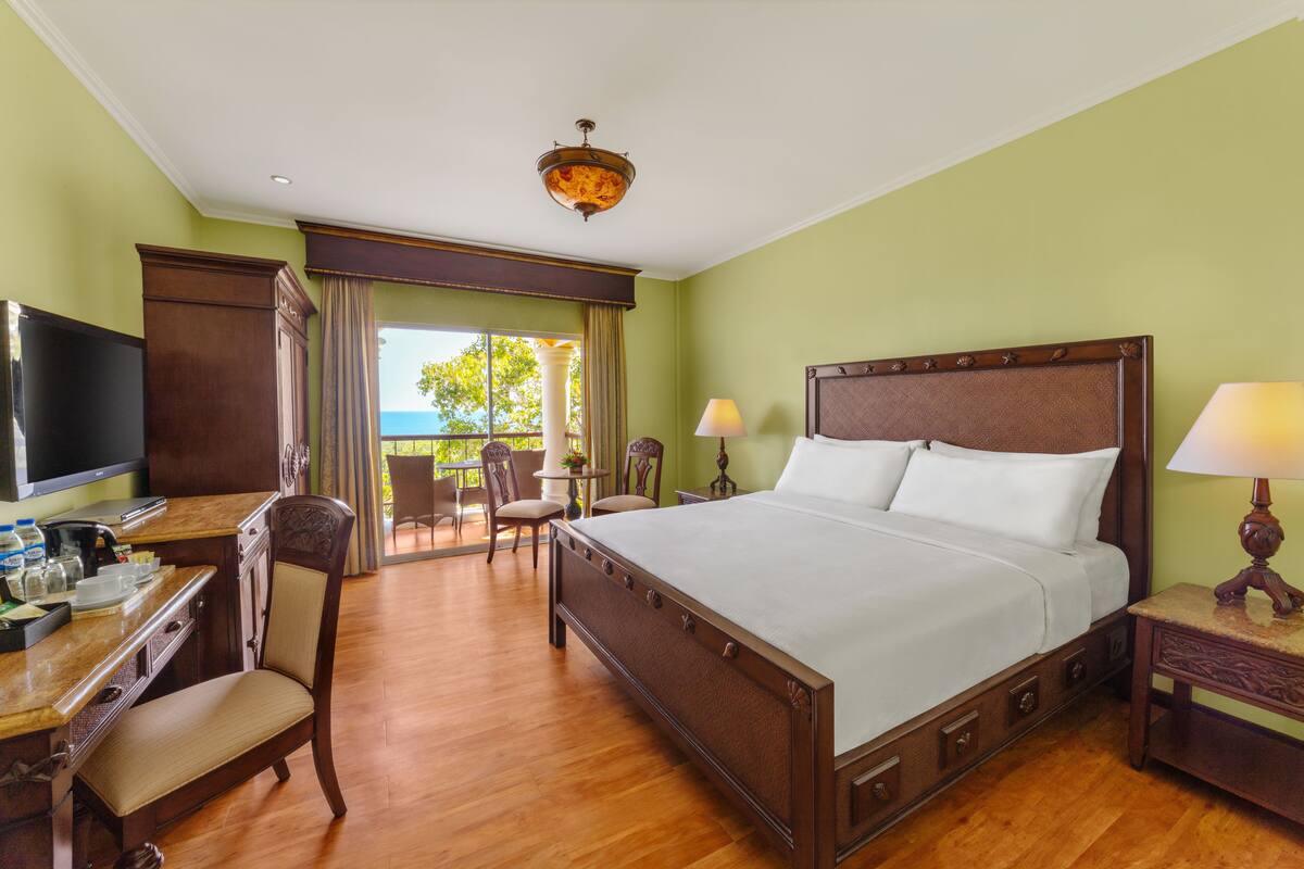 Habitación de hotel con una cama grande, muebles de madera, televisor y vistas al exterior.