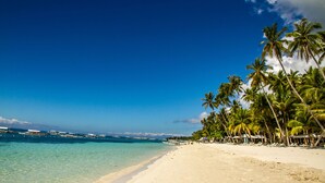 A beach with clear turquoise water, palm trees, and boats. - The Peacock Garden (Baclayon)