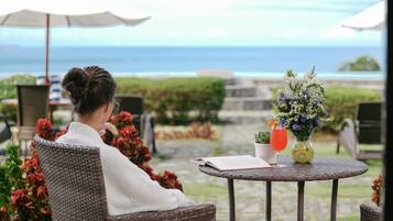 Guests can enjoy a peaceful ocean view from this outdoor seating area, complete with a wicker chair and a small table.