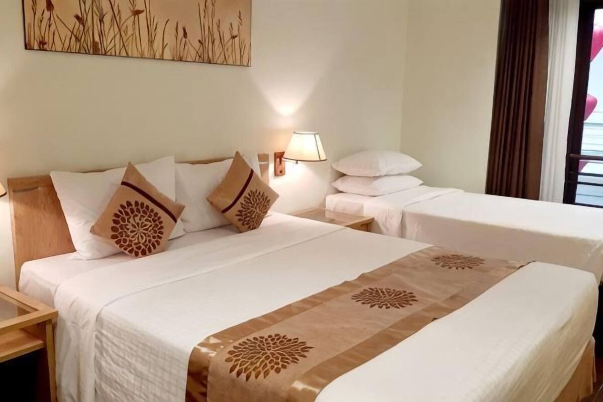 A hotel room with two beds, a nightstand, a lamp, and a painting on the wall.