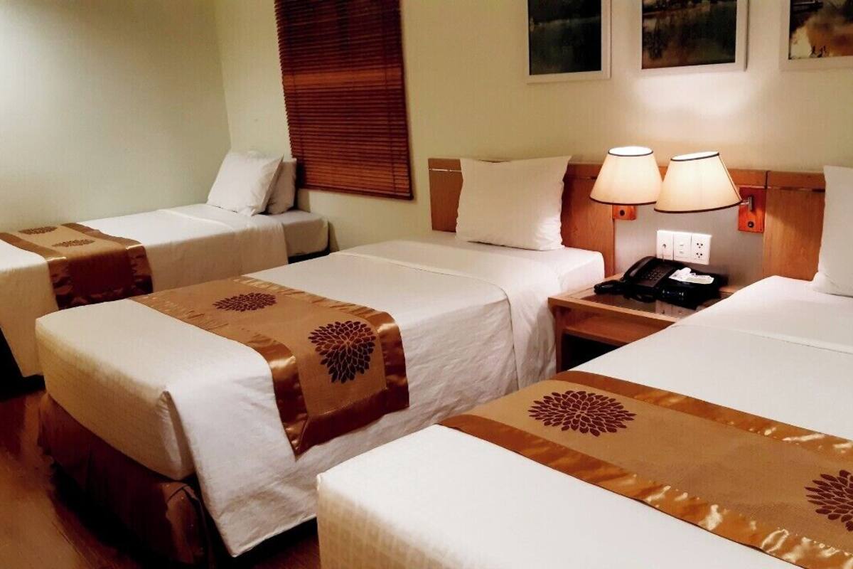 A hotel room with two single beds, a sofa, a nightstand with lamps, and a telephone.