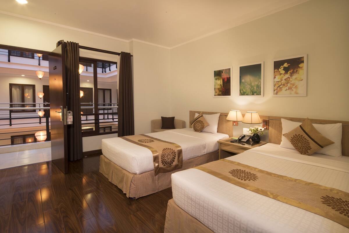 A hotel room with two beds, a wooden floor, a balcony, and a view of the city.