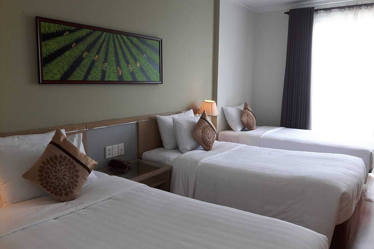 A hotel room with two beds, a painting on the wall, and a window with curtains.