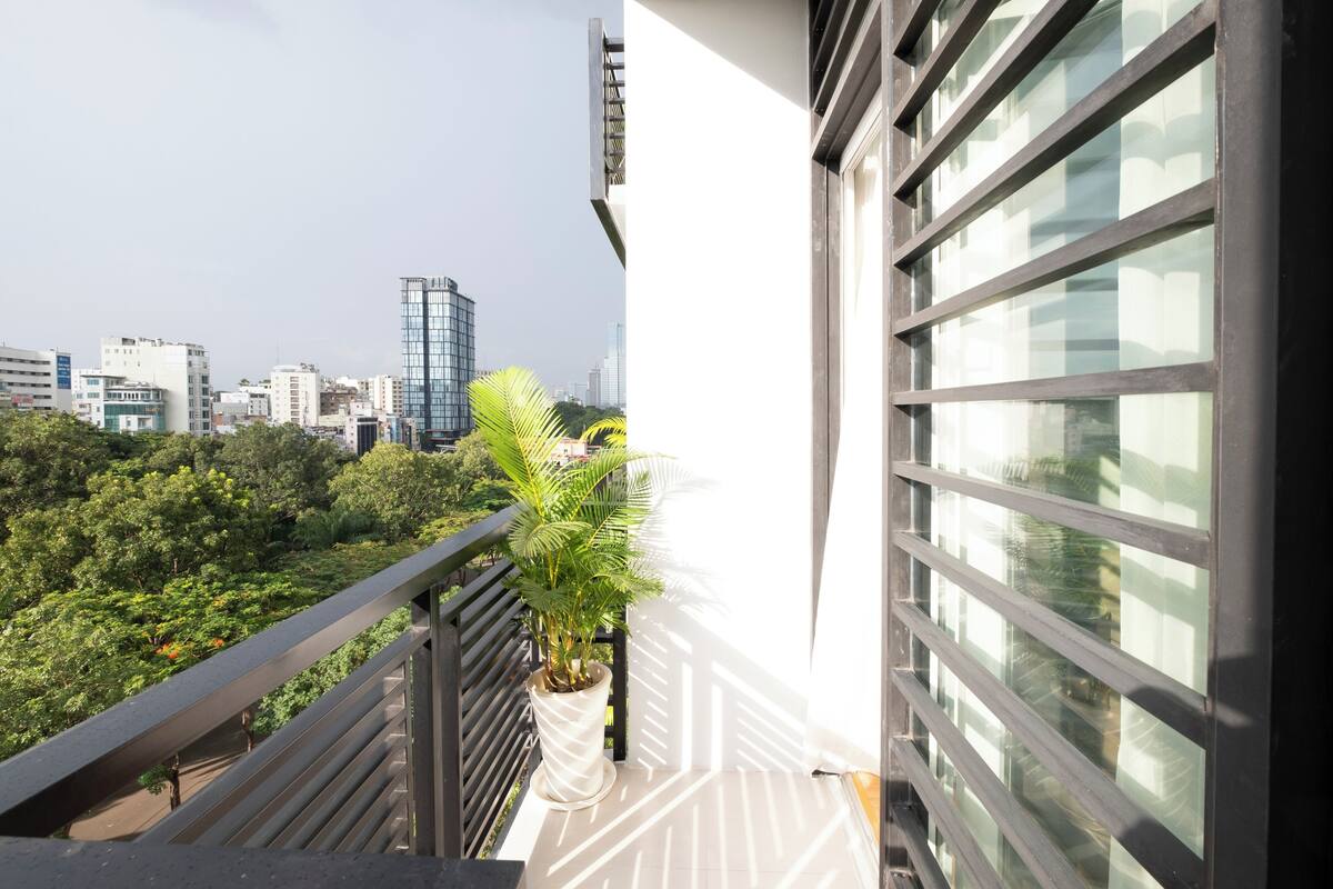 A balcony with a potted plant, a cityscape view, and a modern building facade.