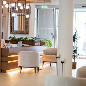 A reception area with a wooden reception desk, a large mirror, and a seating area with two chairs.