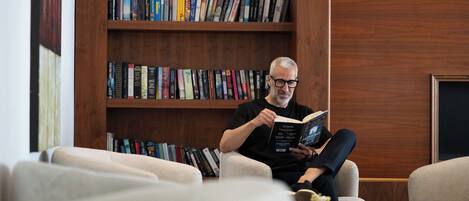 A person sitting on a sofa reading a book in a room with wooden bookshelves filled with books.