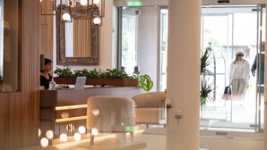 A modern hotel lobby with a reception desk, comfortable seating, and a large window offering a view of the outdoors.