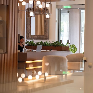 A modern hotel lobby with a reception desk, comfortable seating, and a large window offering a view of the outdoors.