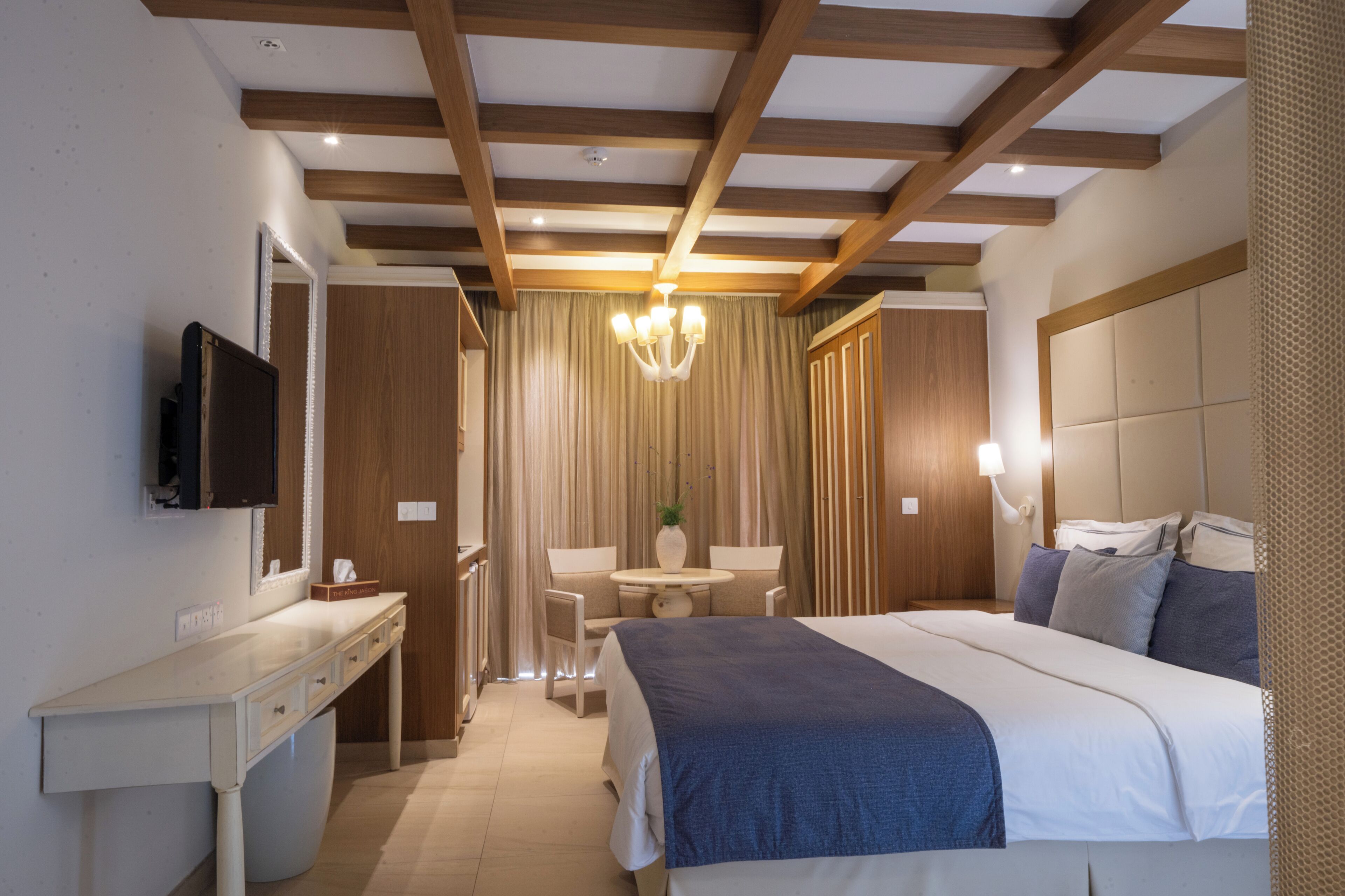 Een slaapkamer met een bed, nachtkastje, televisie en een raam met gordijnen.