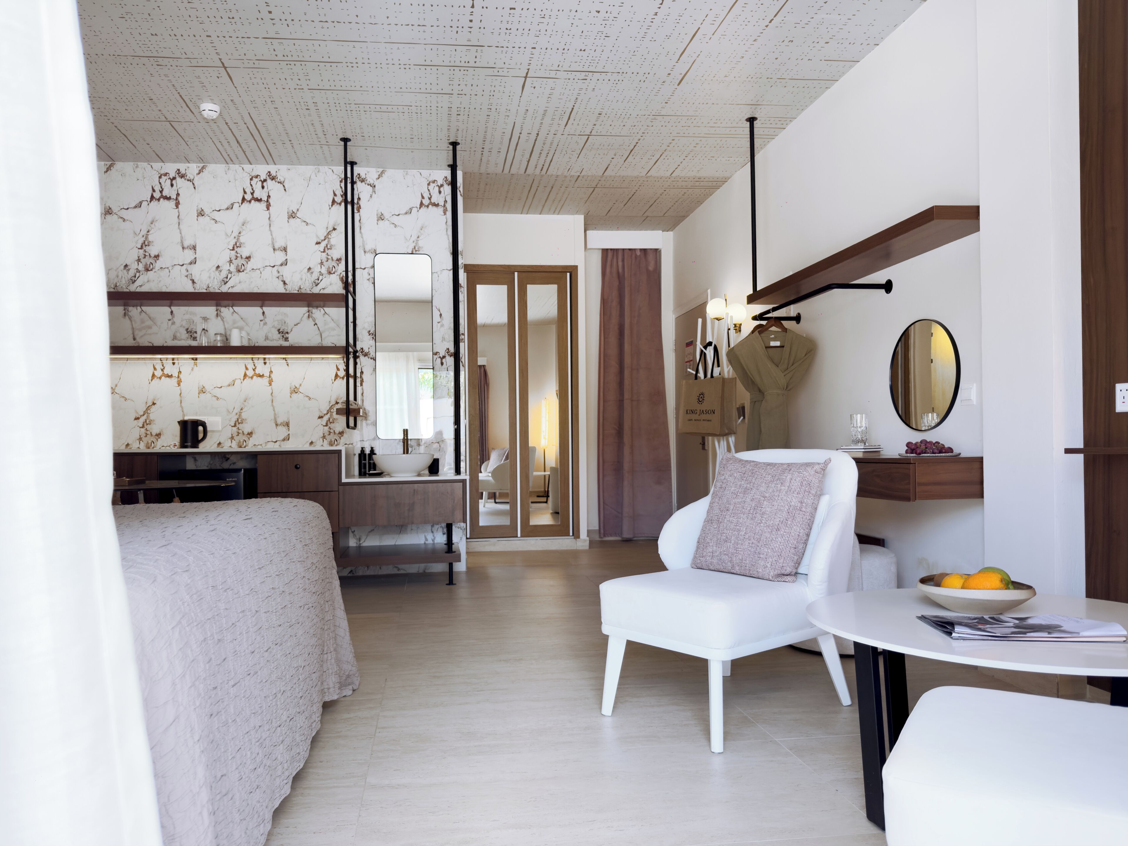 Une chambre d’hôtel moderne équipée d’un lit, d’un coin salon avec une table, d’une coiffeuse avec un miroir et donnant sur le couloir.