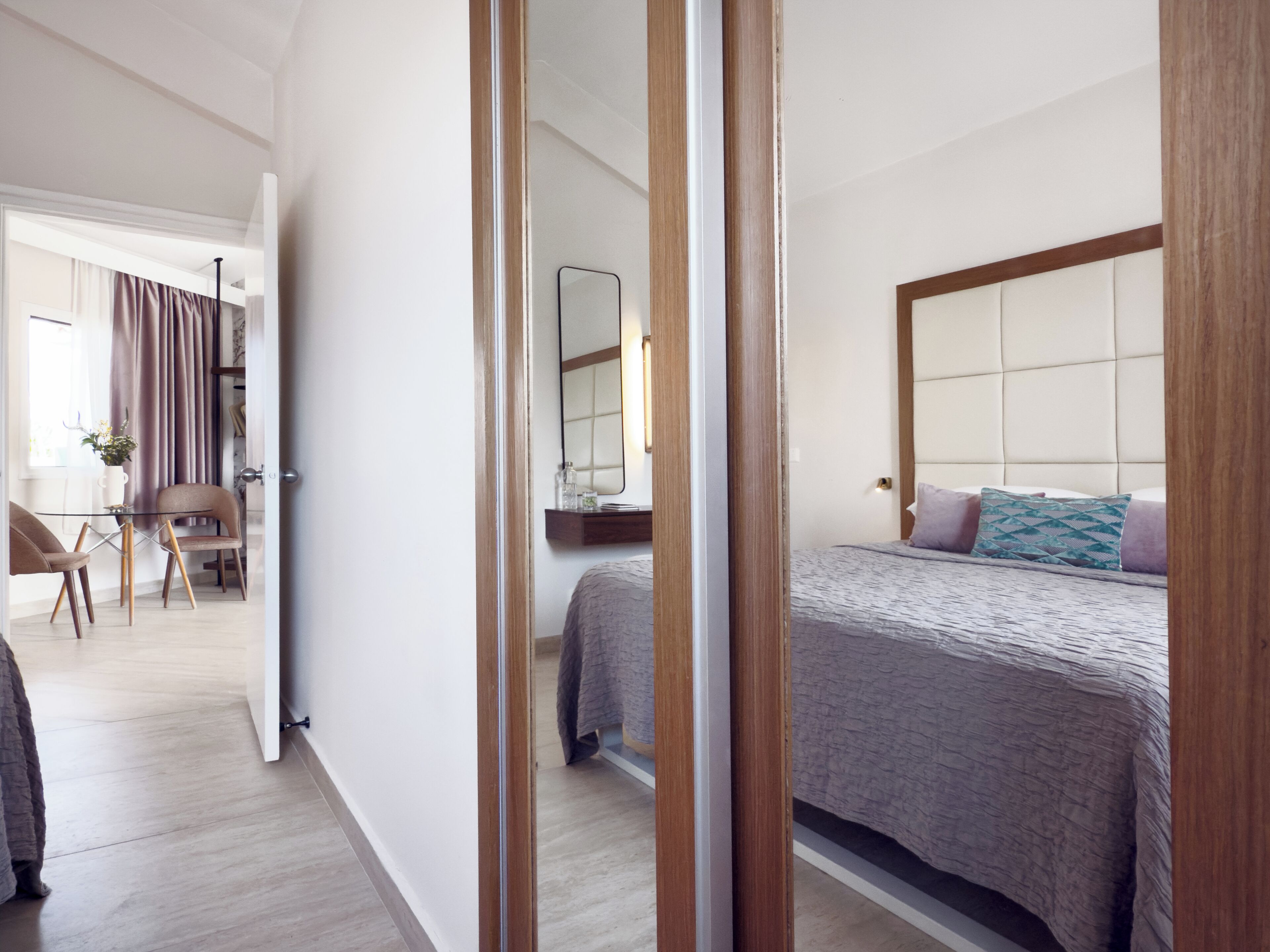 A hotel room with a bed, a bedside table, a mirror, and a view of the hallway.