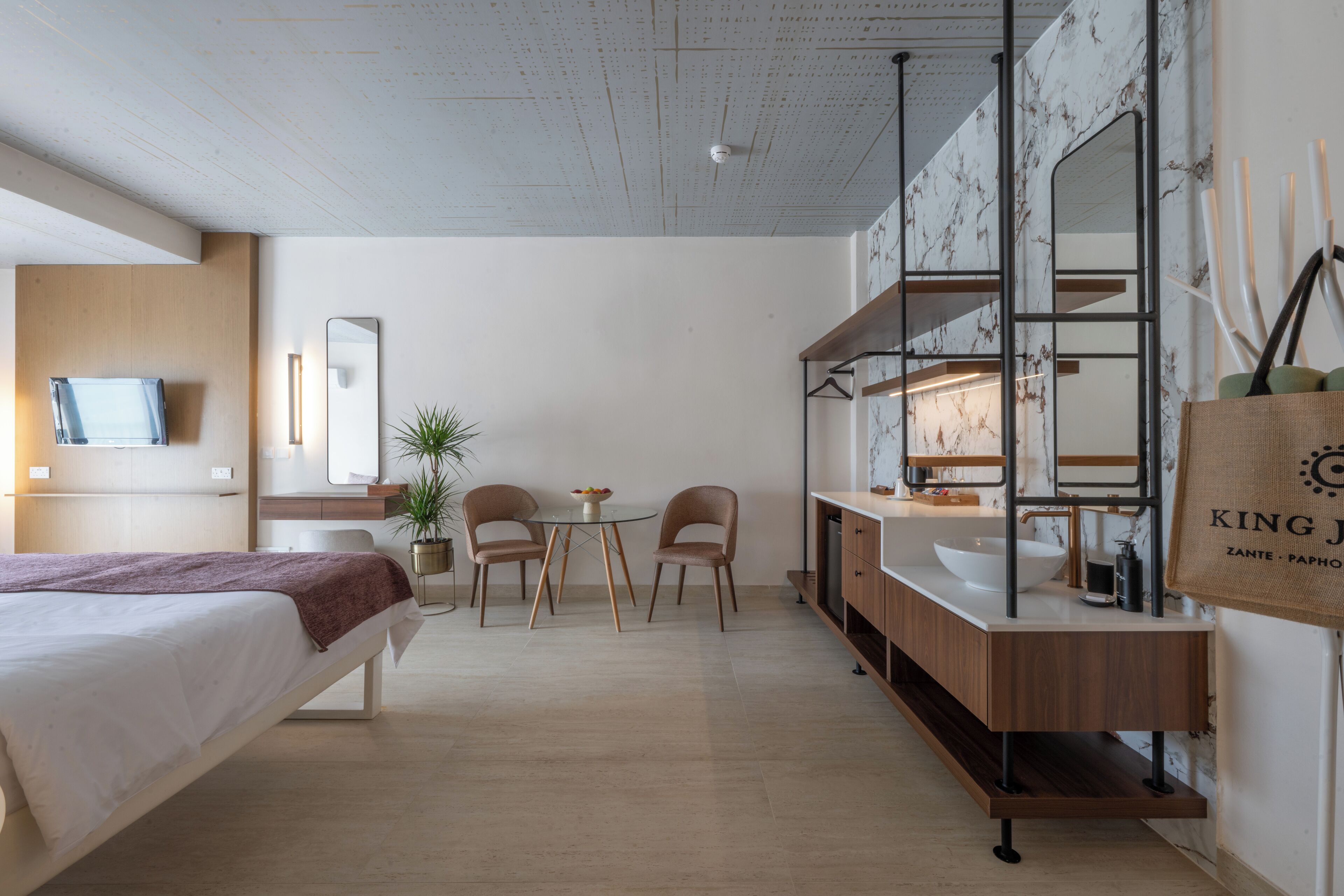 Una habitación de hotel moderna con una cama, un escritorio, una silla, una mesita, un espejo y un baño con lavamanos y espejo.