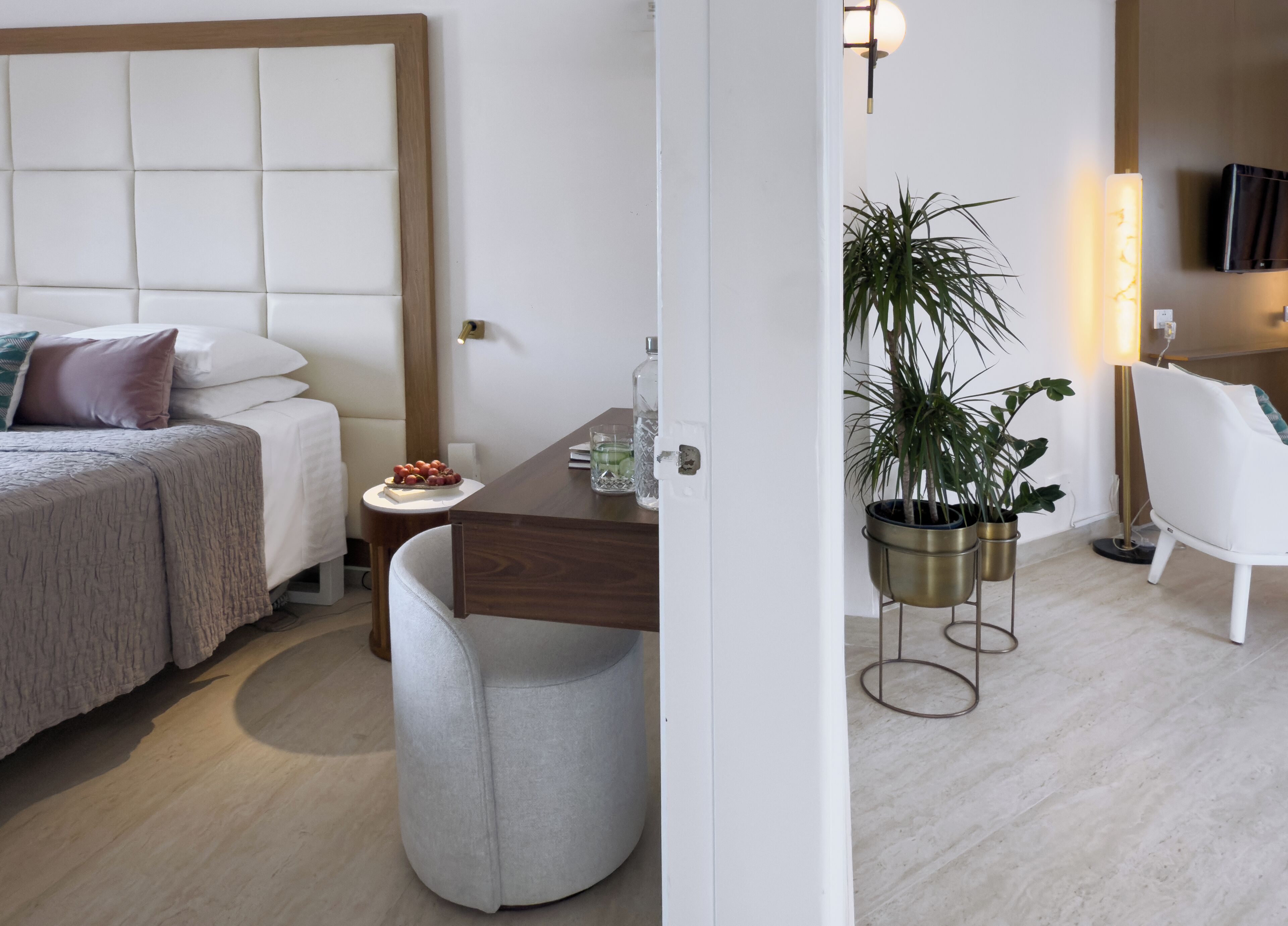 Quarto de hotel com cama, mesa de cabeceira, abajur, cadeira e planta em vaso.