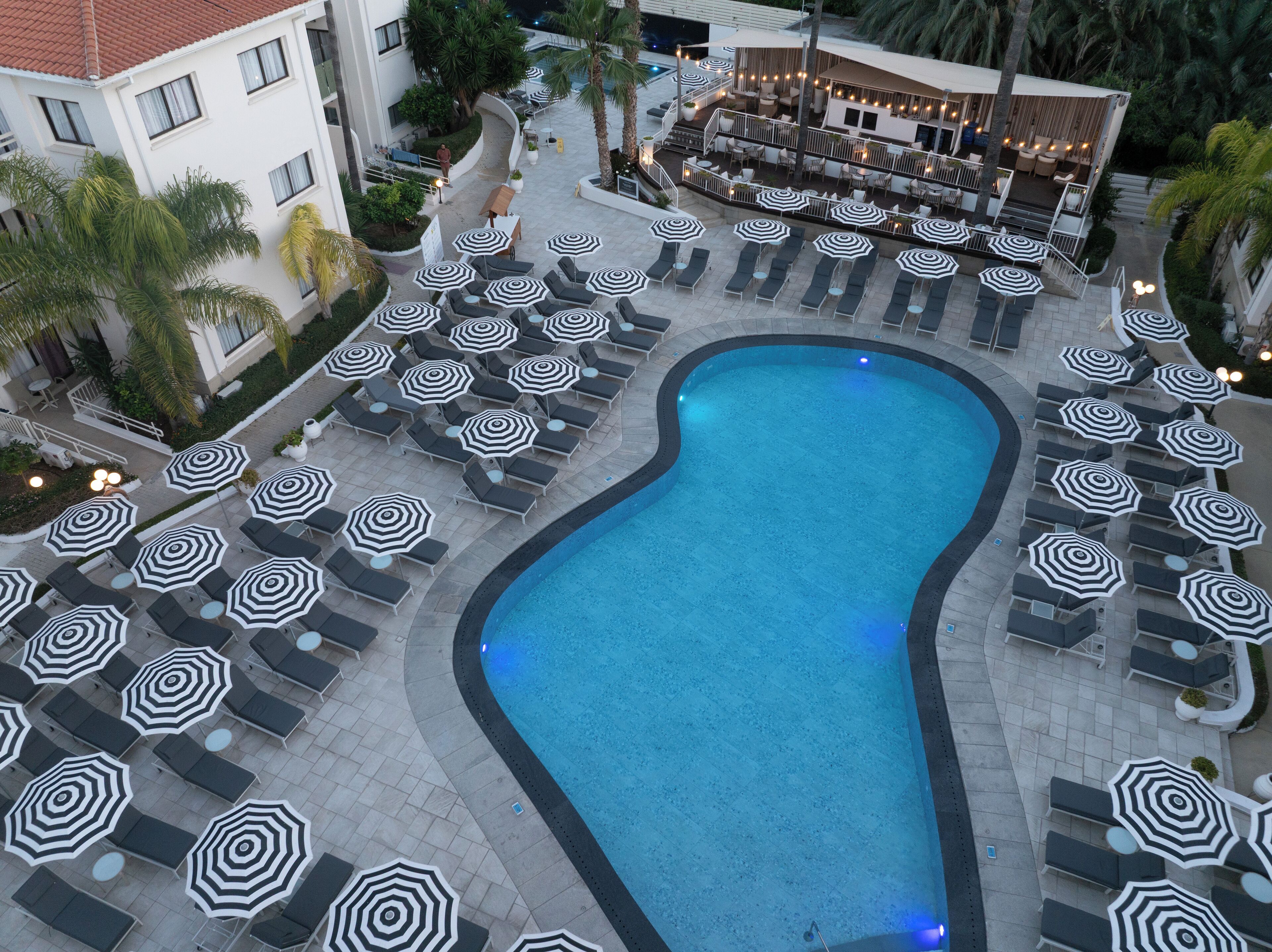 A swimming pool surrounded by lounge chairs and umbrellas, with a restaurant in the background.
