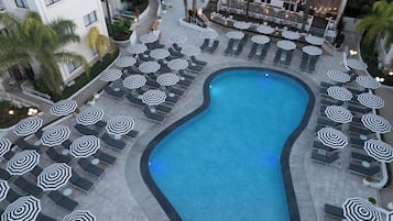A swimming pool surrounded by lounge chairs and umbrellas, with a restaurant in the background.