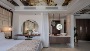 A modern hotel room with a large bed, a vanity with a mirror, a sink, and a ceiling with a unique design.