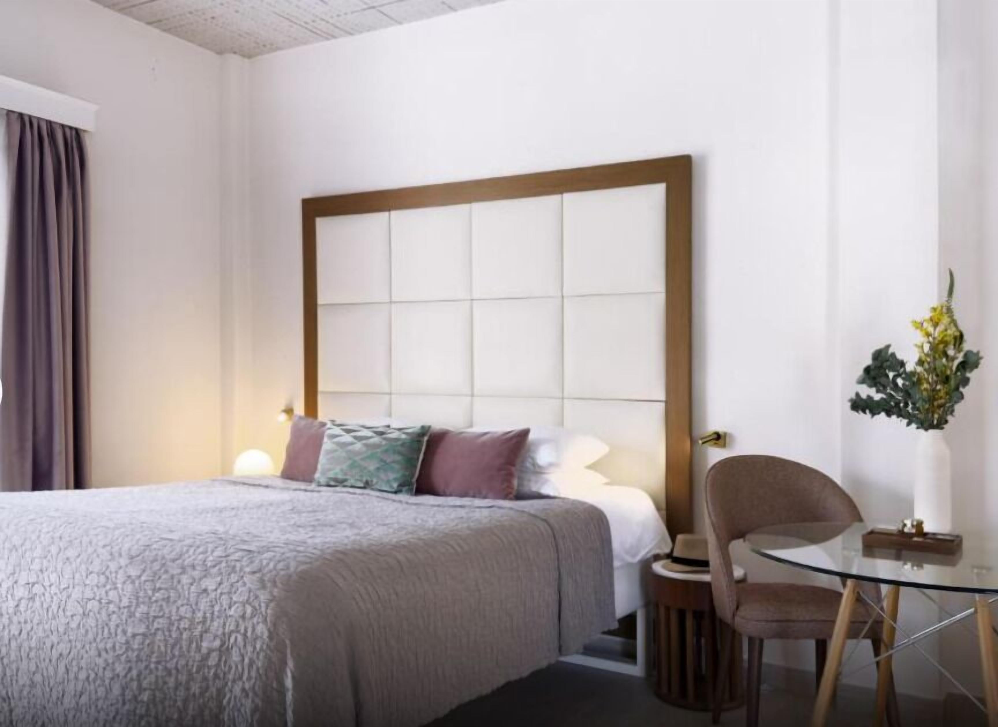 A hotel room with a large bed, a glass table, a chair, and a vase with flowers.