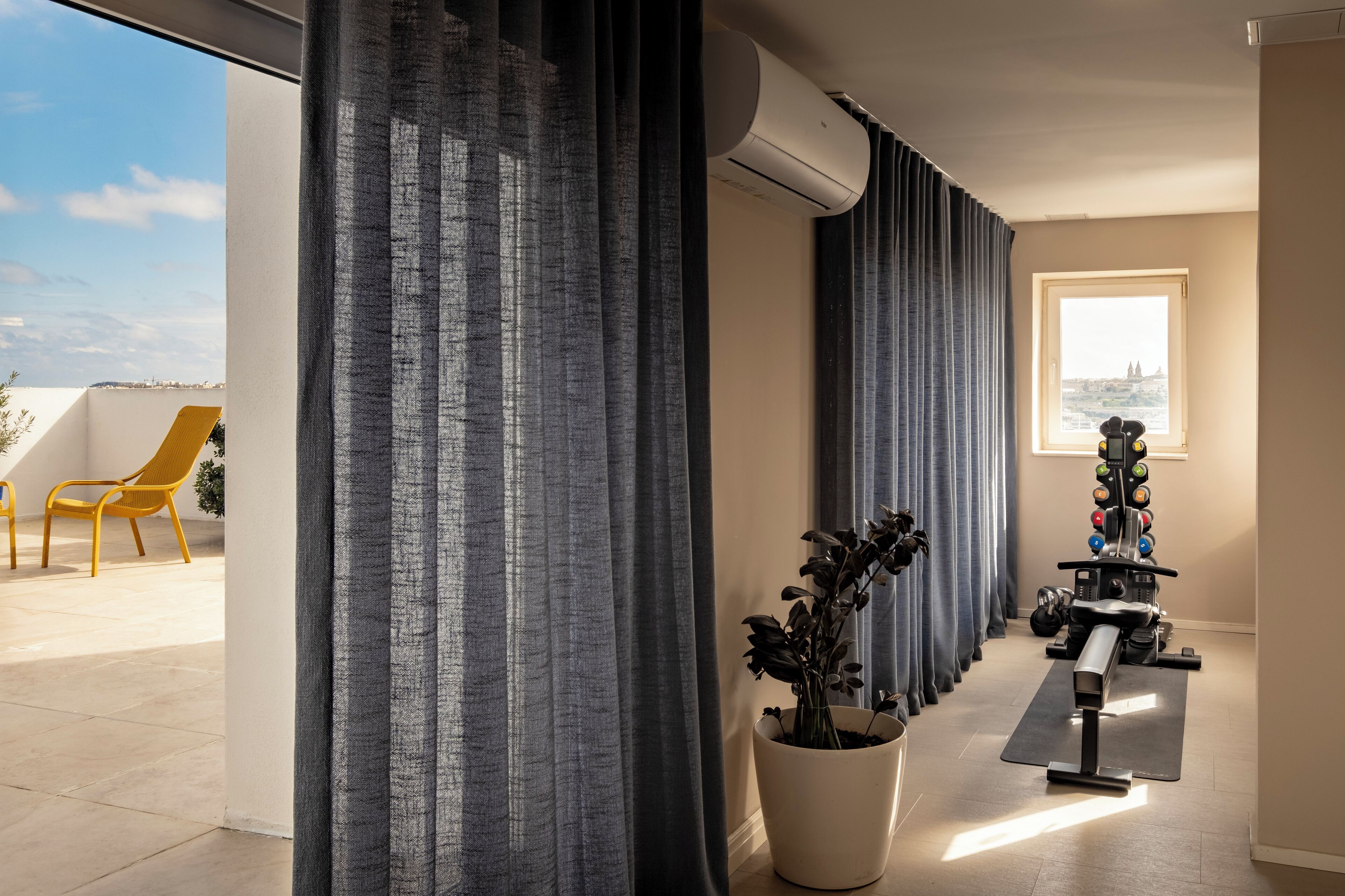 A modern room with a large window, a ceiling fan, a treadmill, and a potted plant.