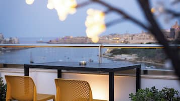 Un balcon avec deux chaises jaunes et une table, d’où l’on peut admirer un paysage urbain et une étendue d’eau.