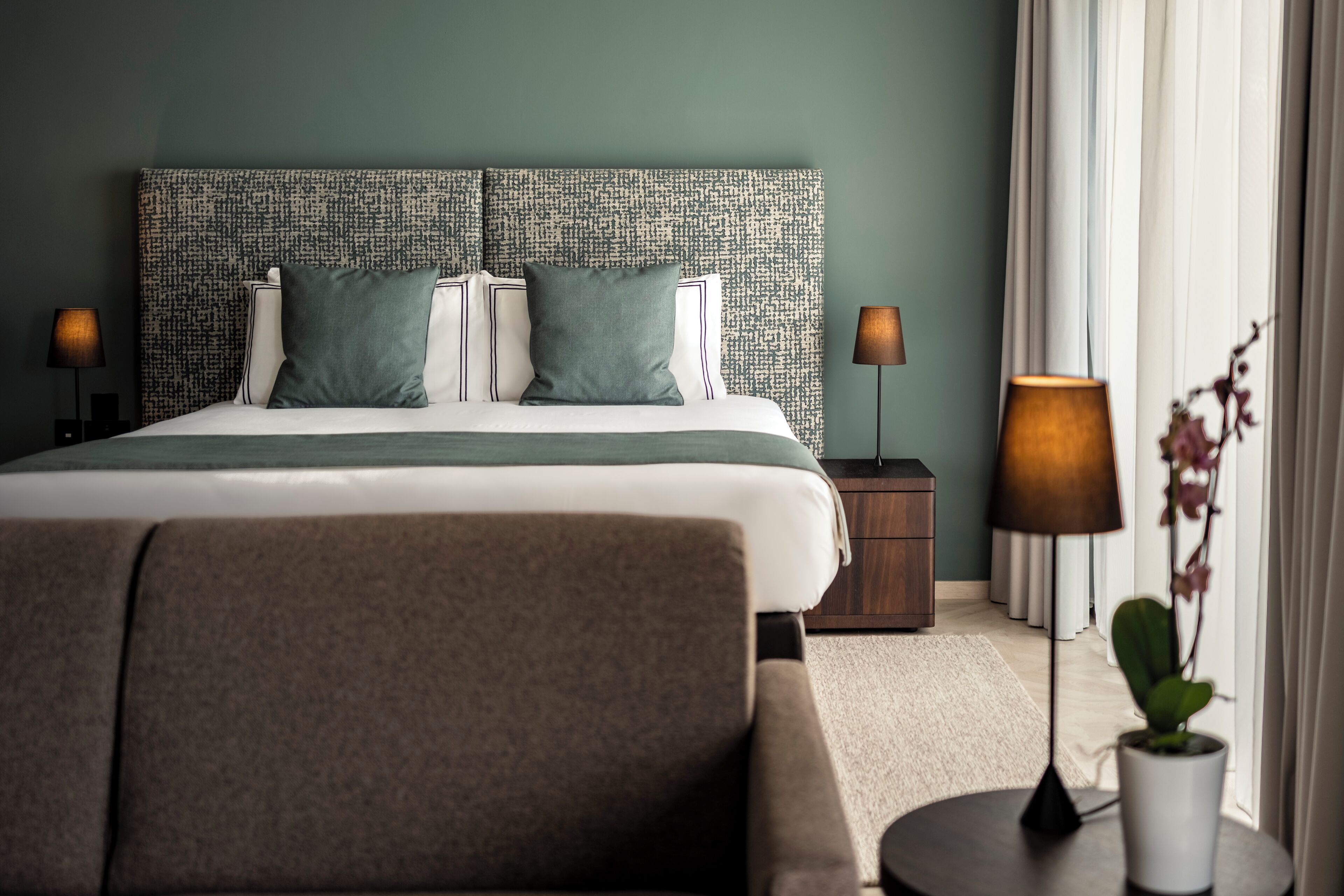 A neatly arranged hotel room with a large bed, two bedside tables, a chair, and a potted plant.