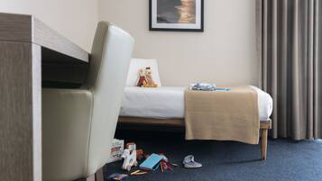 A hotel room with a bed, a chair, a small table, and a window with curtains.