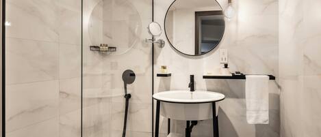 A modern bathroom with a glass-enclosed shower, a round mirror, a white sink, and a towel hanging on a rack.