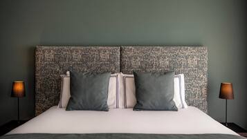 Un lit bien fait, avec une tête de lit à motifs, deux lampes de chevet et un mur de couleur sombre.