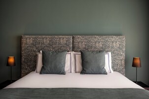 Un lit bien fait, avec une tête de lit à motifs, deux lampes de chevet et un mur de couleur sombre.