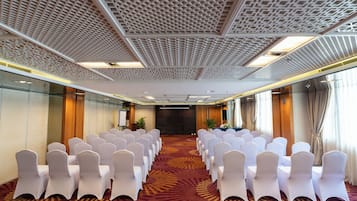 A conference room with rows of white chairs and a patterned carpet.