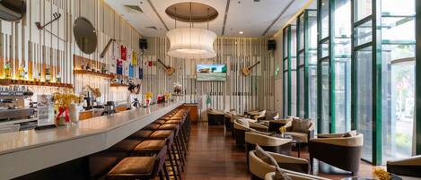 Un bar moderno con una barra alargada, varios taburetes y un espacio de estar con sofás y mesas.