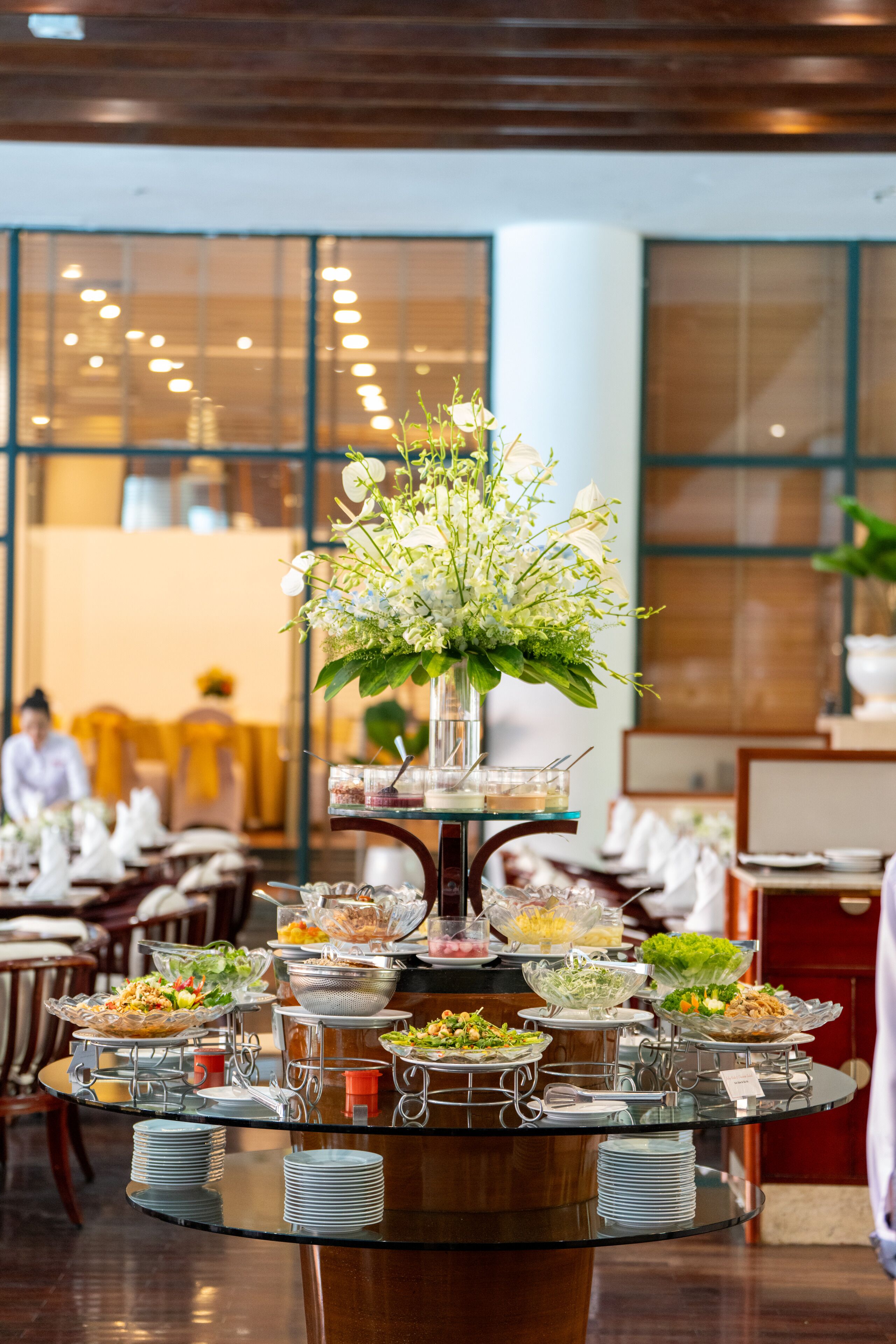 A buffet setup with various food stations and a centerpiece of white flowers in a glass vase.