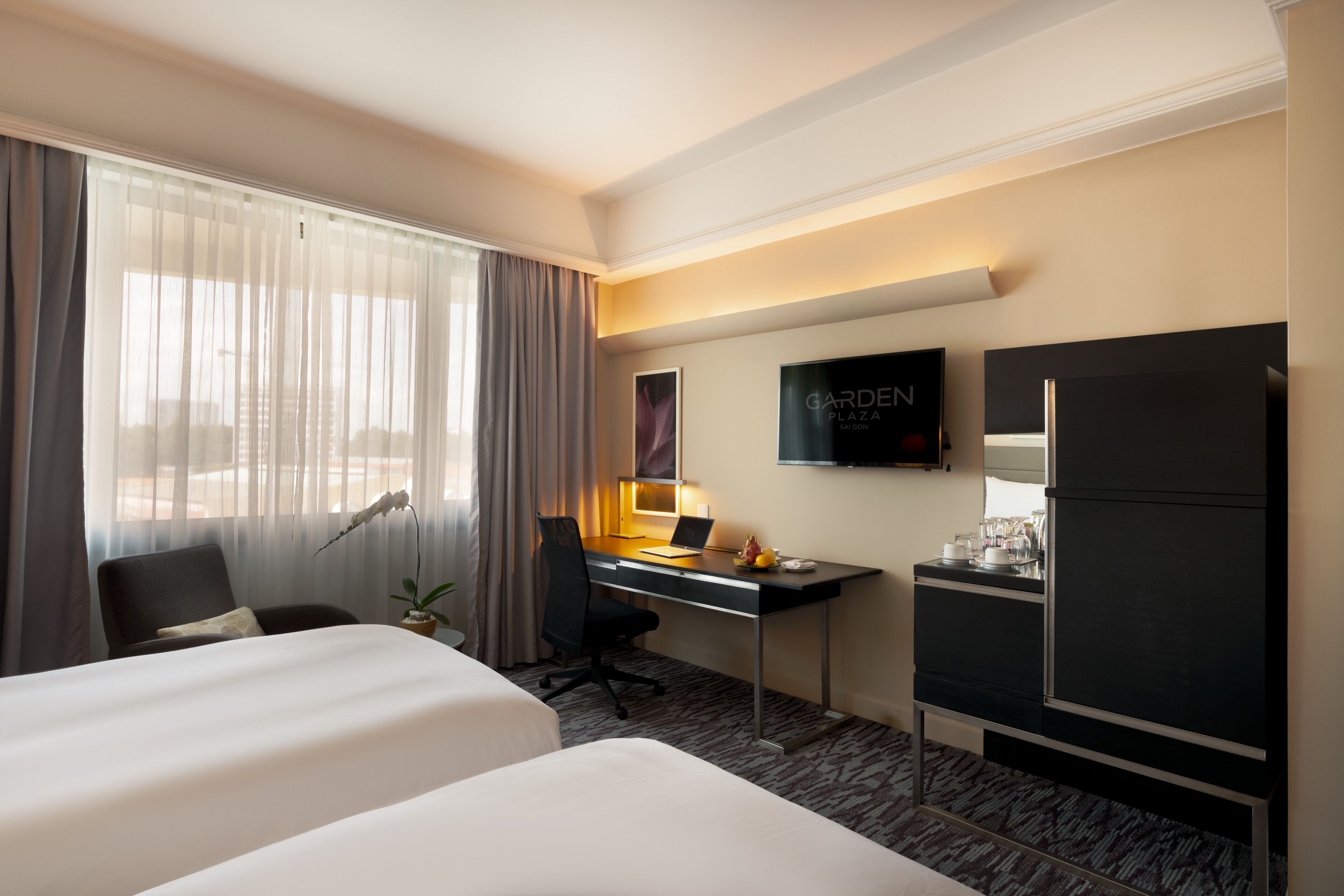 A hotel room with a bed, desk, chair, TV, and a minibar.