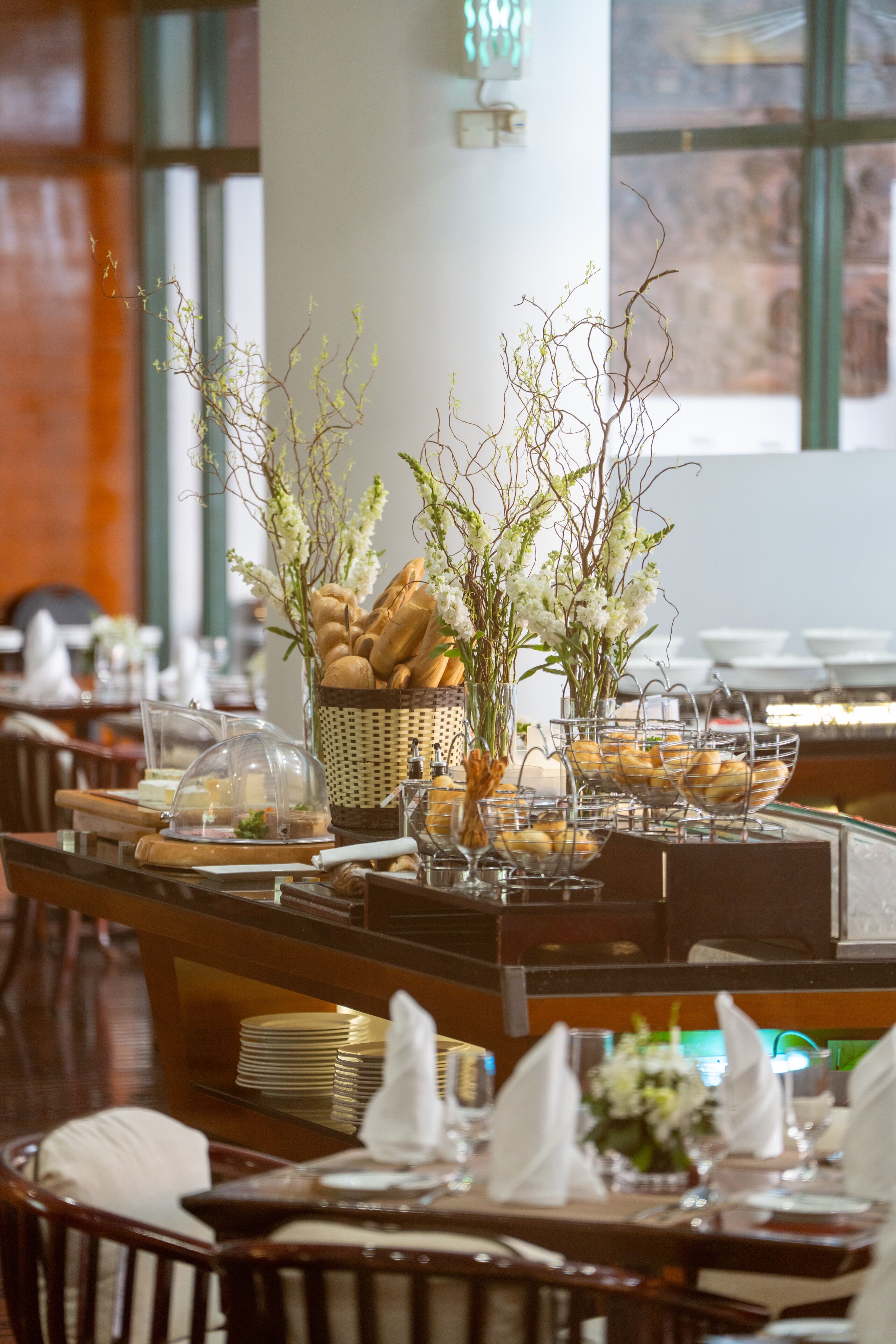 A buffet setup with bread baskets, clear glass bowls, and white napkins on tables.