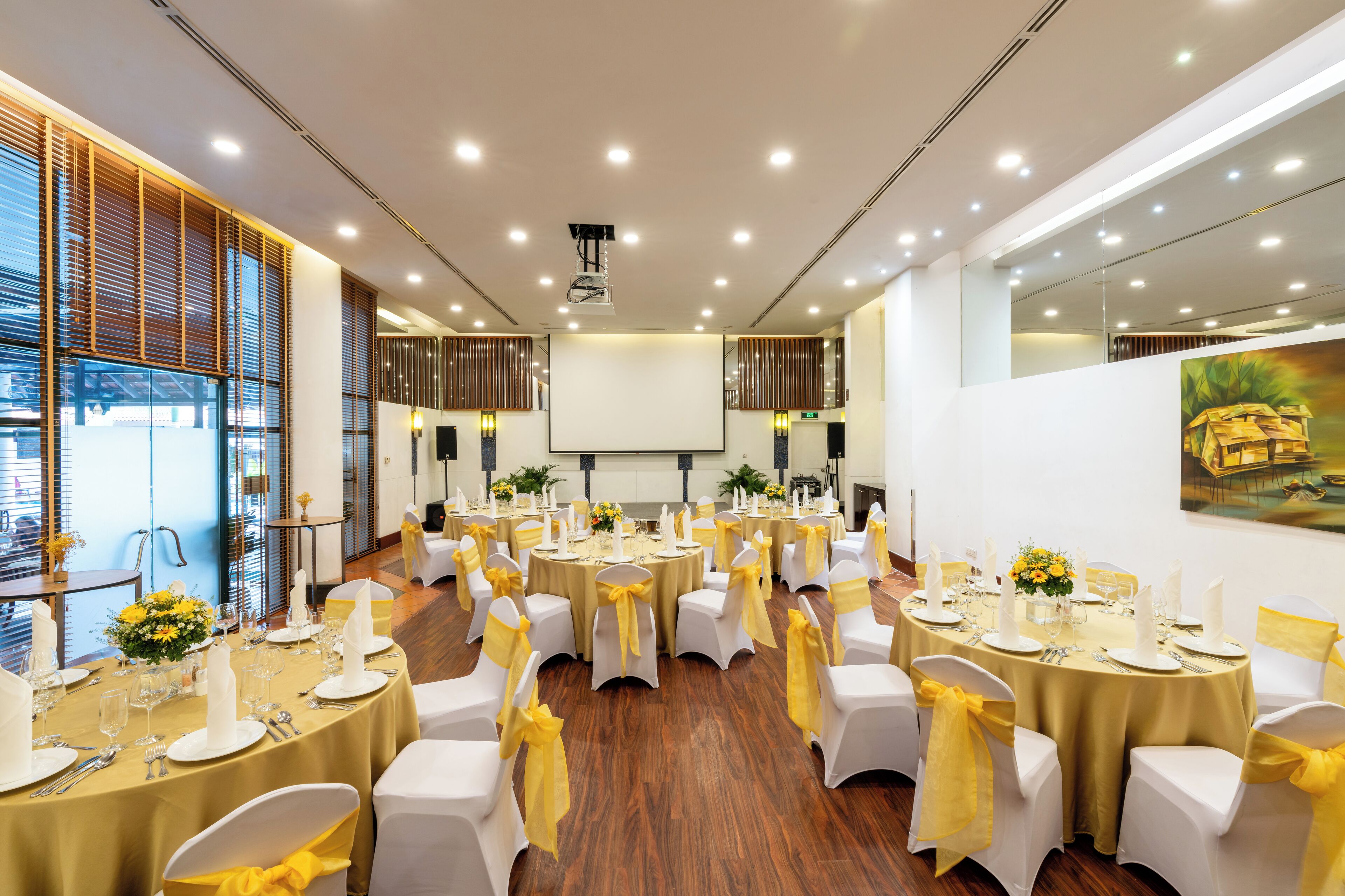 A conference room with multiple round tables, each set with white chairs and yellow sashes, and equipped with candles and floral centerpieces.