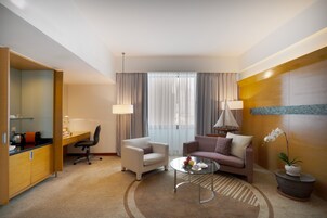 Una habitación de hotel moderna con escritorio, dos sillas, un sofá, una mesita de centro y una orquídea en maceta.