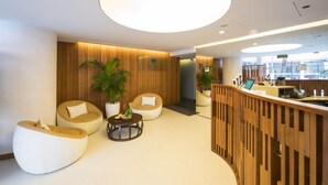 Un espace d’accueil moderne, doté d’un comptoir de réception en bois, de sièges confortables et d’un grand luminaire circulaire.