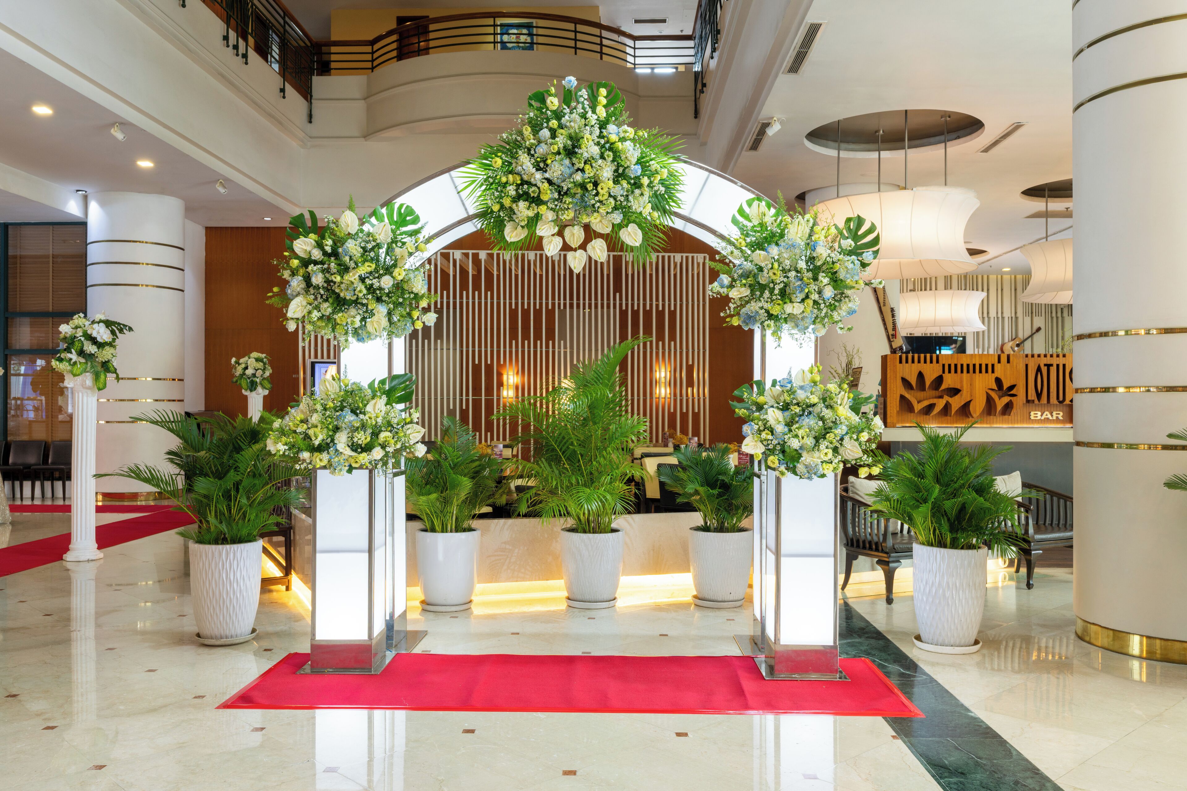 A hotel lobby with a red carpet, white columns, and floral decorations.