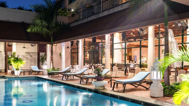 Un espace aménagé au bord de la piscine, avec des chaises longues, une piscine et un coin salon intérieur doté de grandes fenêtres.